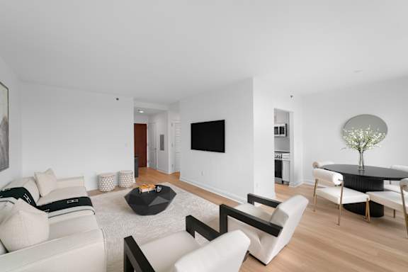 A modern living room with a white couch, a black coffee table, and a TV on the wall.