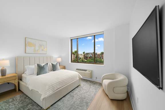 A bedroom with a large bed, a chair, and a flat screen TV mounted on the wall.