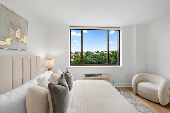 A bedroom with a large bed and a view of the outdoors through a large window.