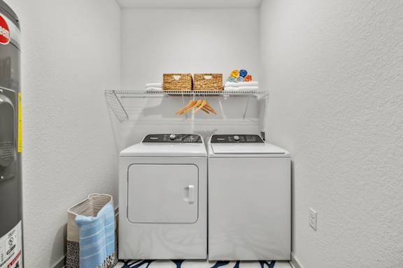 A white laundry room with a washer and dryer and a shelf with food on it.