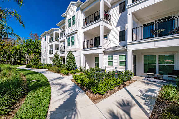 A white apartment building with green bushes and a walkway in front.