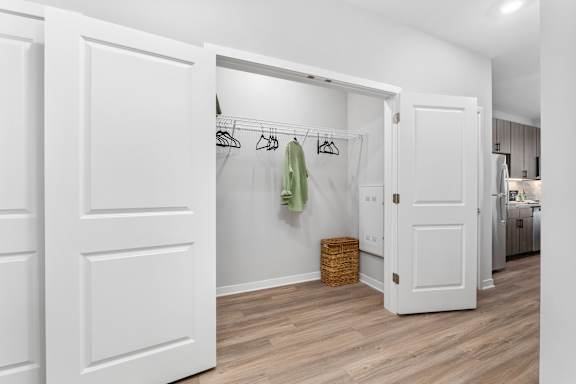 A white closet with a basket and clothes hanging on a rail.