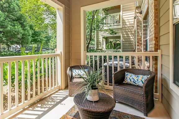 A balcony with a wicker chair and table with a potted plant on it.