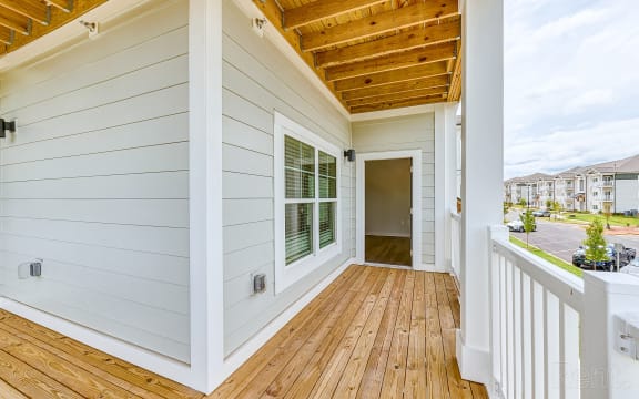a porch with a wooden floor and a white house with a door