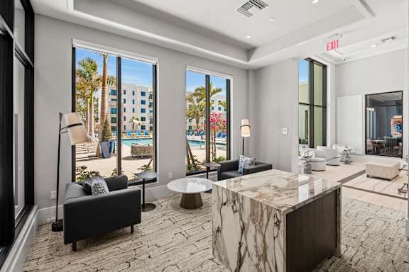 A modern living room with a marble table and a view of a pool and palm trees.