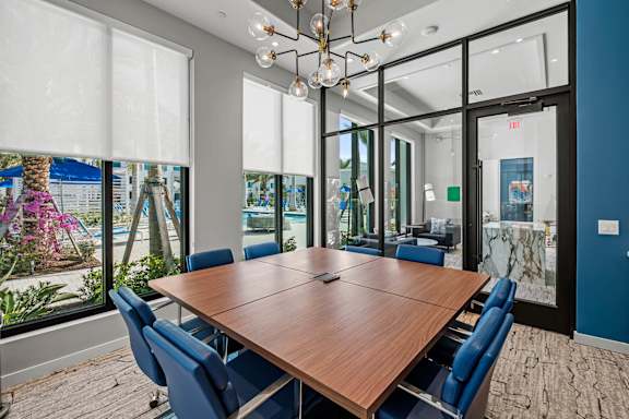 A conference room with a long table and chairs, a chandelier, and a view of the outside through the windows.