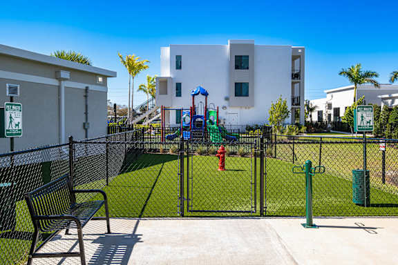 A playground area with a slide, swings, and a bench in front of a white building.
