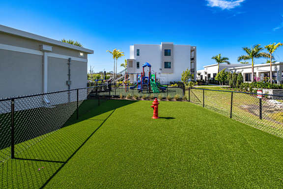 A playground with a red fire hydrant in the middle of a green lawn.