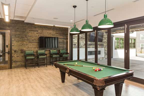A pool table with green lampshades hanging from the ceiling.