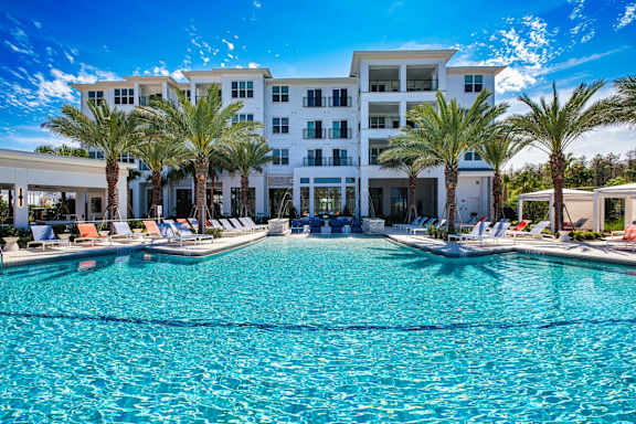a large swimming pool with palm trees in front of a building at Altis Twin Lakes Apartments, Kissimmee, Florida