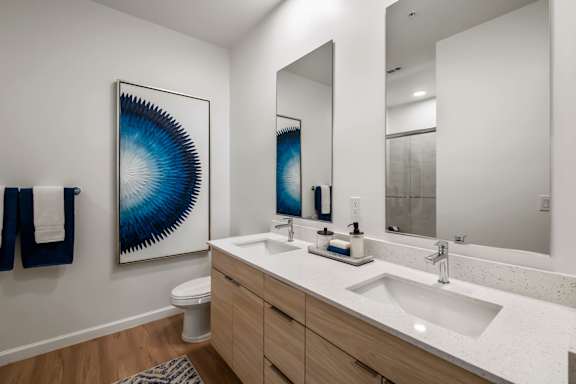A bathroom with a white counter top and a blue and white painting hanging on the wall.