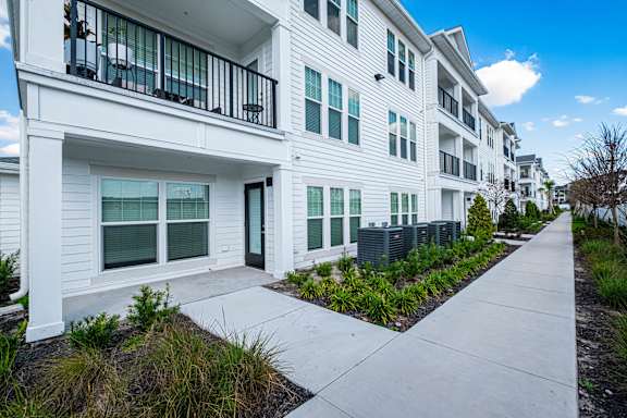 A white apartment building with a balcony and a walkway in front.