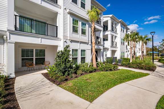 A white apartment building with a balcony and a palm tree in front.