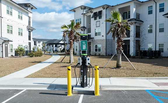 A charging station for electric vehicles is located in a parking lot in front of apartment buildings.