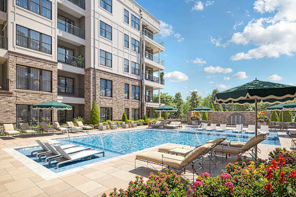 A large swimming pool with sun loungers and umbrellas in front of a multi-story apartment building.