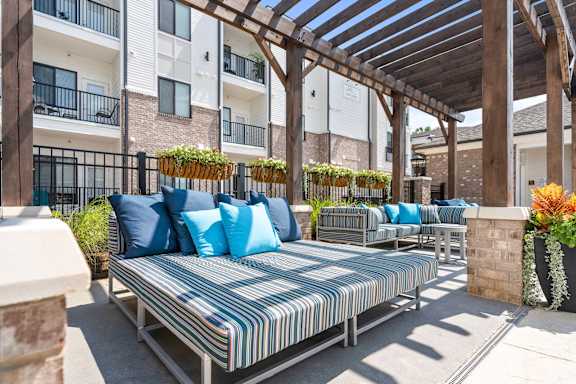 A patio with a striped cushion sofa and a wooden pergola.
