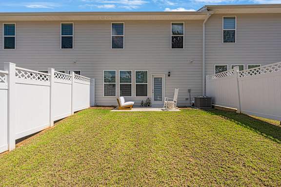 A white fence surrounds a small lawn in front of a two-story house.