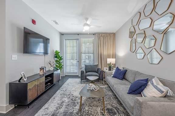 A living room with a grey couch, a wooden cabinet, and a TV mounted on the wall.