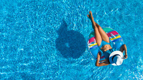A woman in a blue bikini and hat floats on a pool with her feet in the air.