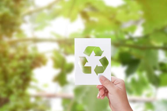 A hand holding a paper with a recycling symbol on it.