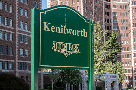 A green sign that says Kenilworth Alden Park stands in front of a building.