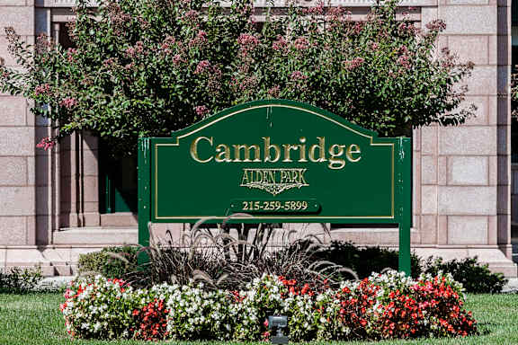 A green sign that says Cambridge Aiden Park in front of a building.