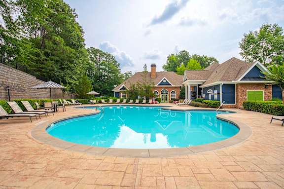 A large swimming pool surrounded by a brick patio and lounge chairs.