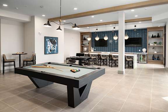 A pool table is in the middle of a room with a bar and a TV.