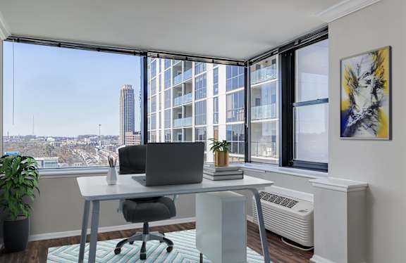 A modern home office with a laptop on the desk and a view of the city.