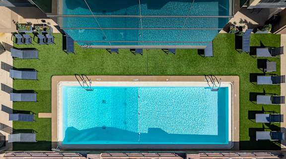A rectangular pool surrounded by lounge chairs and green grass.