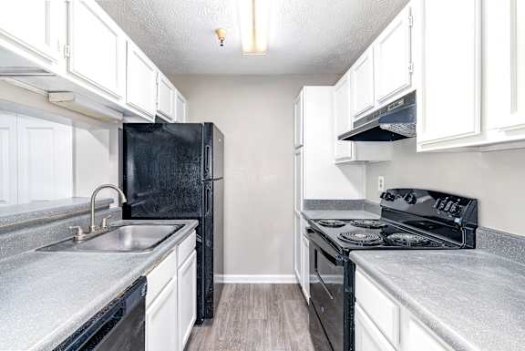 A black refrigerator sits in a kitchen with white cabinets.