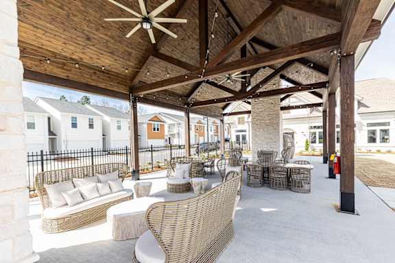 A patio with a wicker sofa and chairs under a wooden roof.
