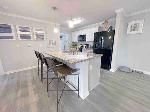 A kitchen with a black fridge, white cabinets, and a marble countertop.