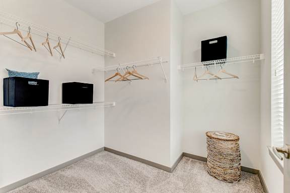A room with a white wall and a shelf with clothes hangers and a black box.