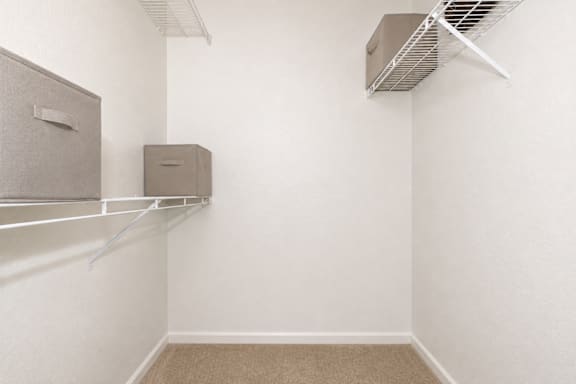 A room with a carpeted floor, a white wall, and a metal shelf with two storage boxes.