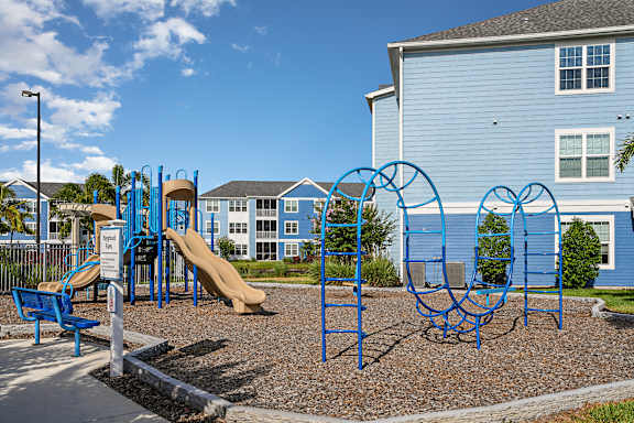 A playground with a blue slide and swings in front of a blue building.