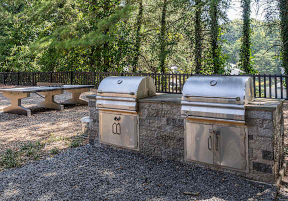 Three outdoor grills are lined up on a gravel area.