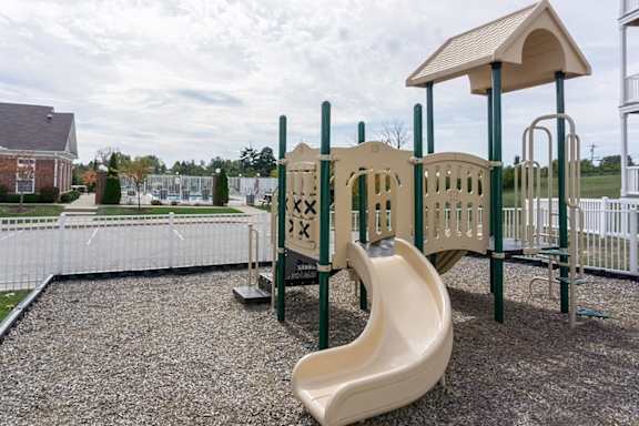 A playground with a yellow slide and a white fence.