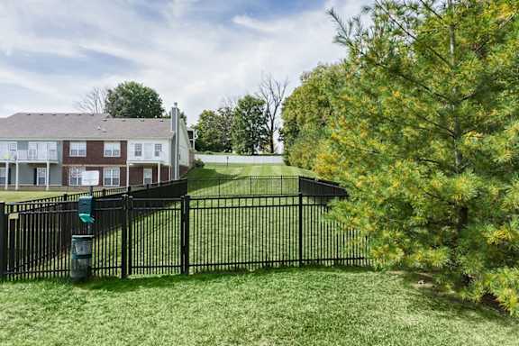 A black fence surrounds a green lawn in front of a brick building.