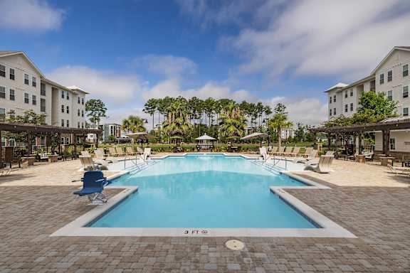 A large swimming pool surrounded by a brick patio and lounge chairs.