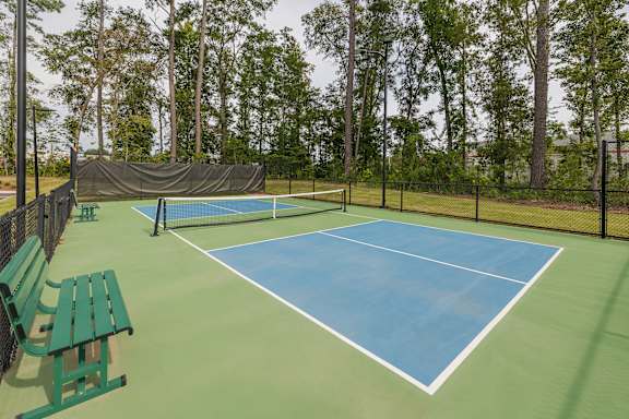 A tennis court with a green bench and a black fence.