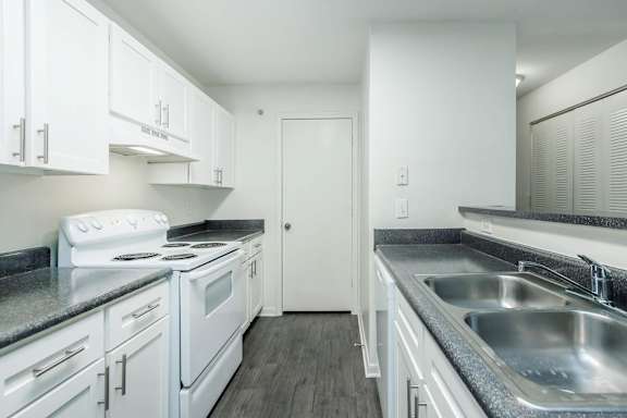 A white kitchen with a stove top oven and a sink.