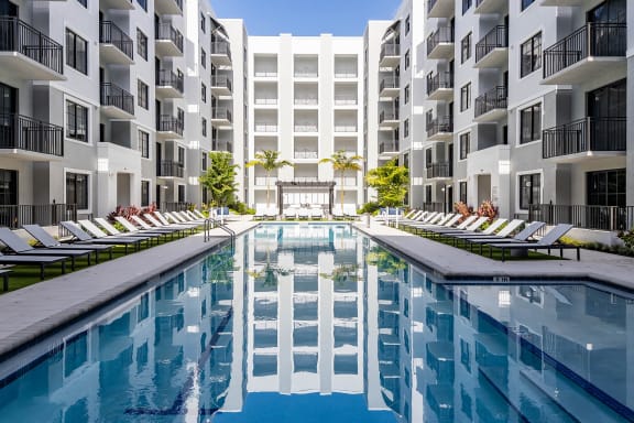 an outdoor pool with lounge chairs and a white building in the background at Leena Plantation, Plantation, FL