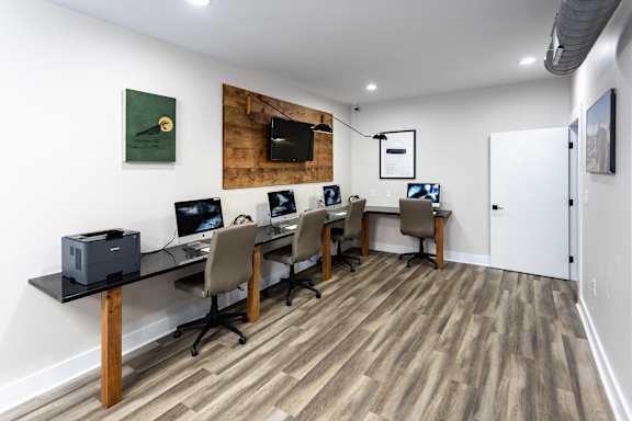 a room with a row of computers on a table and a tv on the wall