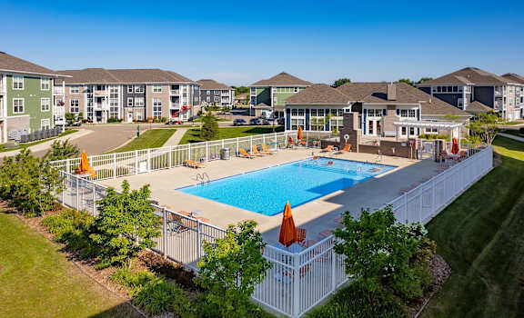 A large swimming pool surrounded by a white fence and a grassy area with trees.