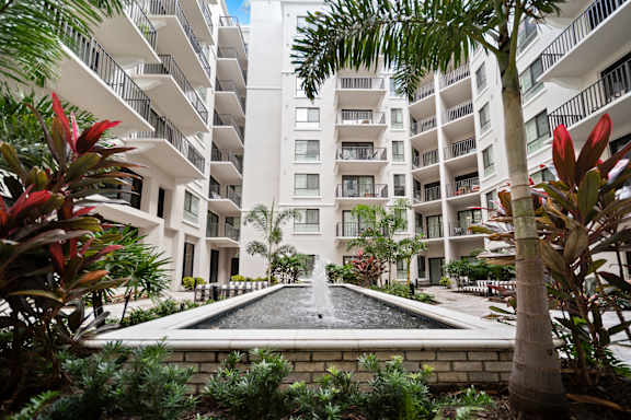 A fountain in the middle of a courtyard surrounded by buildings and plants.
