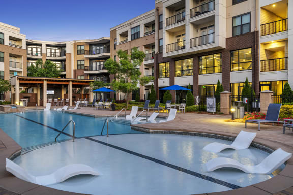 a swimming pool with lounge chairs in front of an apartment building
