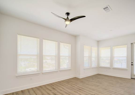 A room with a ceiling fan and windows with blinds.