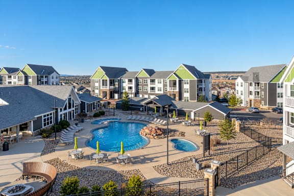 A large outdoor swimming pool surrounded by a black fence and a small patio area with a table and chairs.
