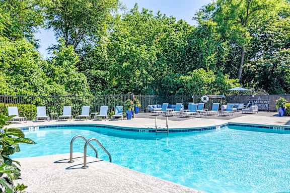 A pool surrounded by trees and chairs.